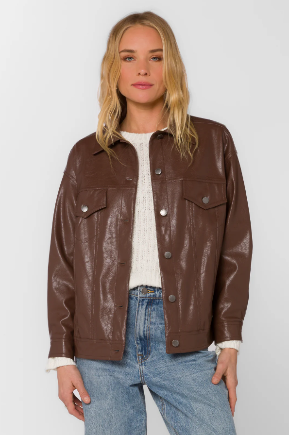 Woman wearing a brown faux leather jacket over a white sweater with a plain background
