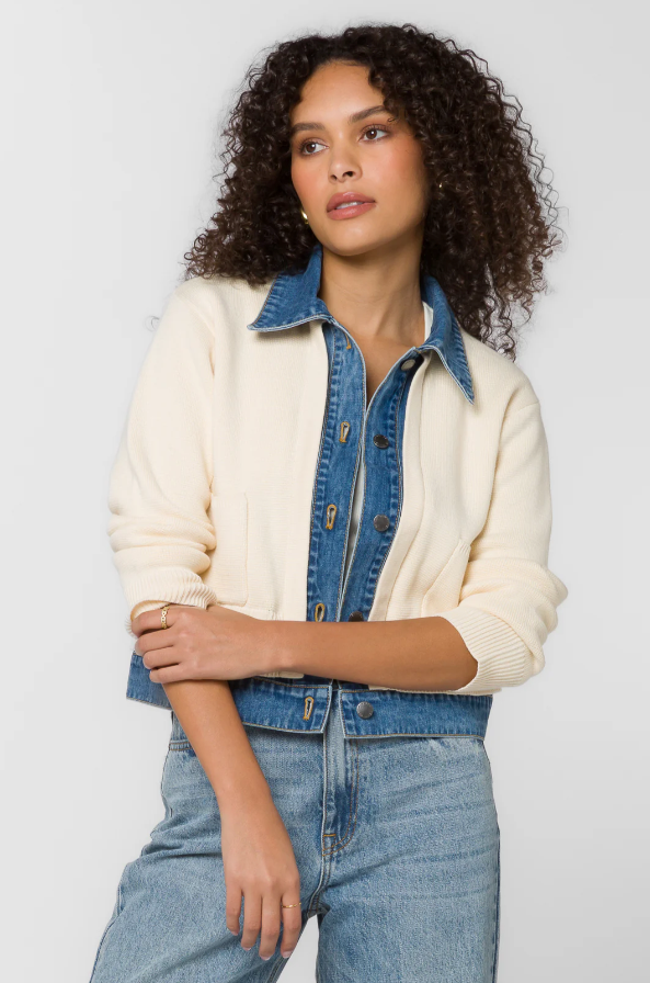 Woman wearing a cream and denim jacket with blue jeans on a light gray background