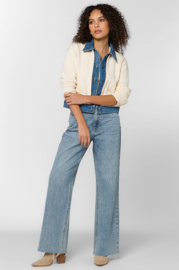 Woman wearing a cream and denim jacket and jeans on a white background