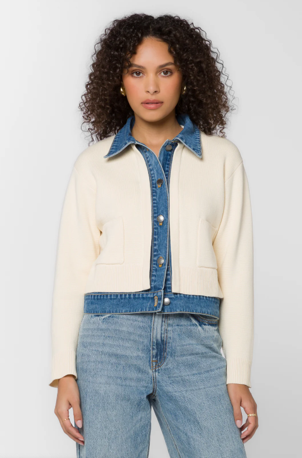 Person wearing a cream jacket with denim collar and jeans on a plain background