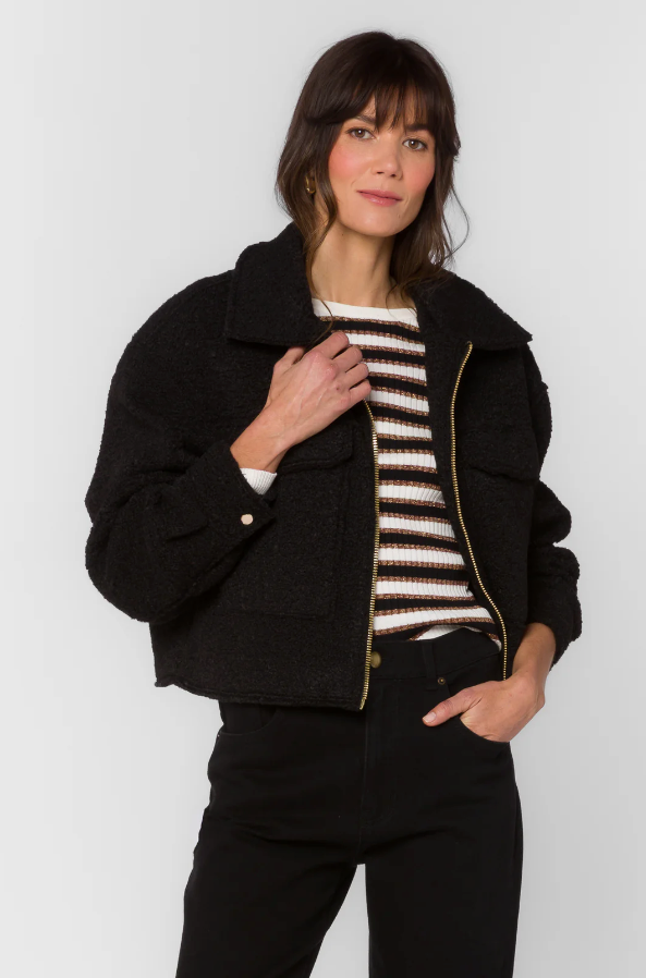 Woman wearing a black jacket over a striped sweater on a white background