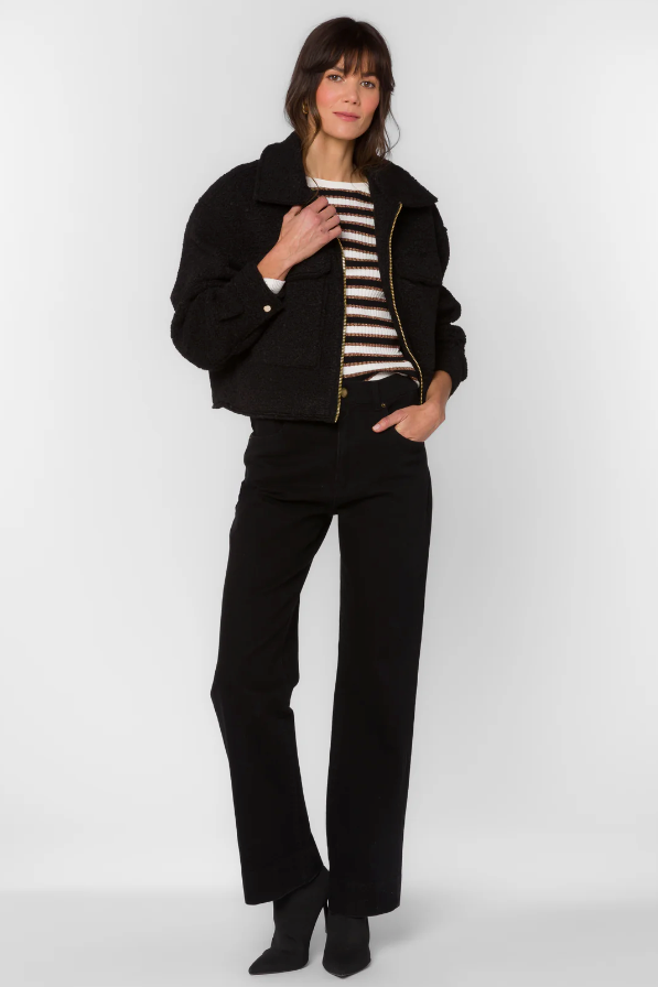 Woman wearing a black jacket and pants with a striped shirt on a white background