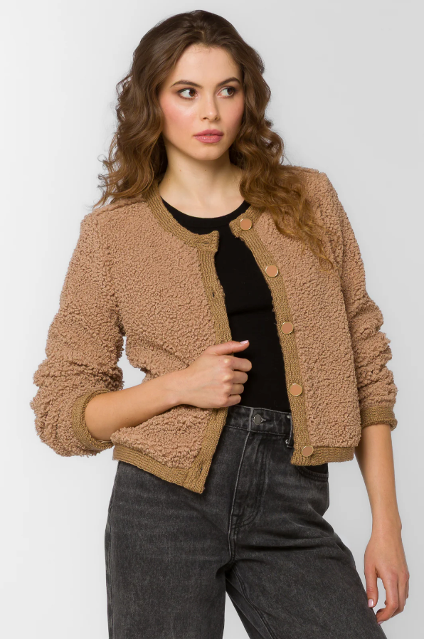 Woman wearing a brown jacket over a black top and dark jeans on a white background