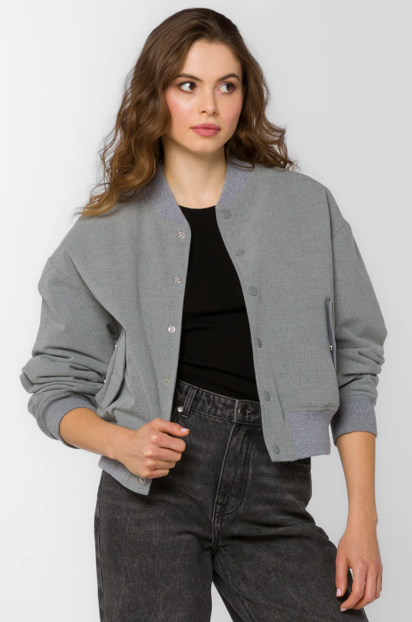 Woman wearing a gray bomber jacket over a black top and jeans on a white background