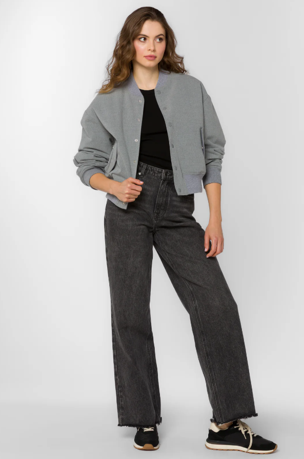 Woman wearing a gray bomber jacket, black top, and dark jeans on a white background
