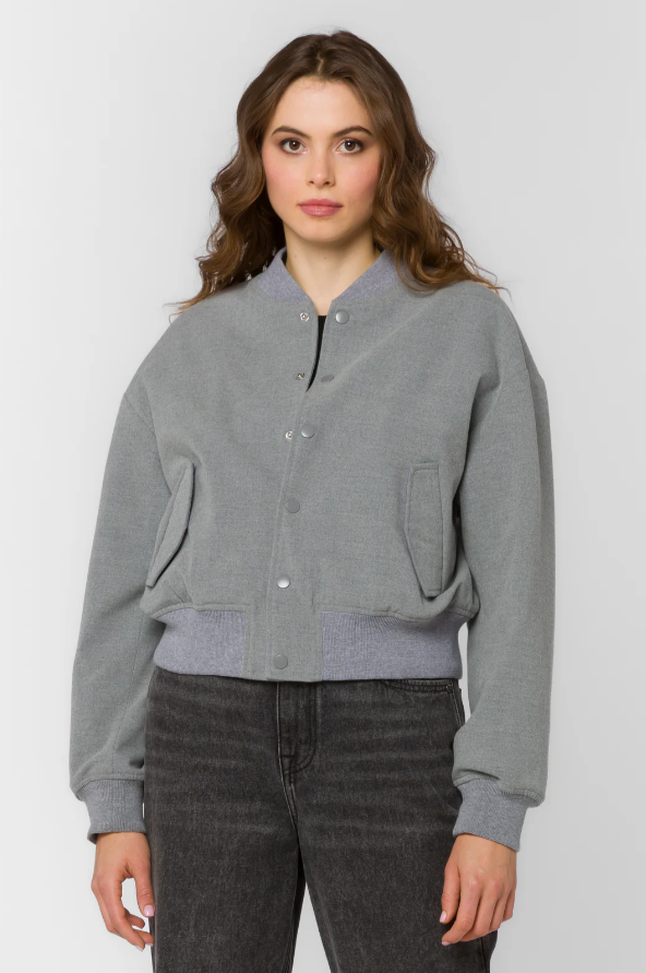 Woman wearing a gray bomber jacket with dark jeans on a white background