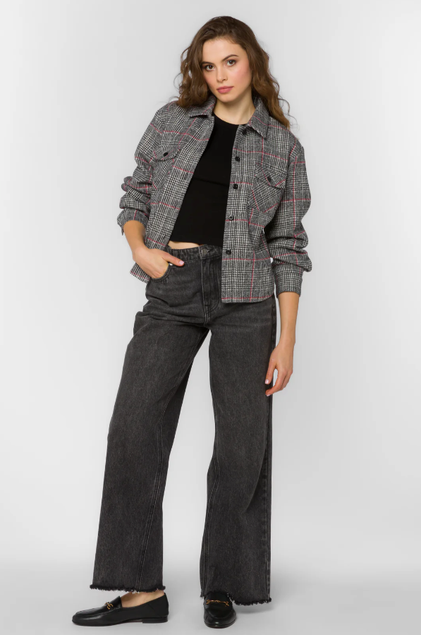 Woman wearing a plaid jacket, black top, and dark jeans on a white background