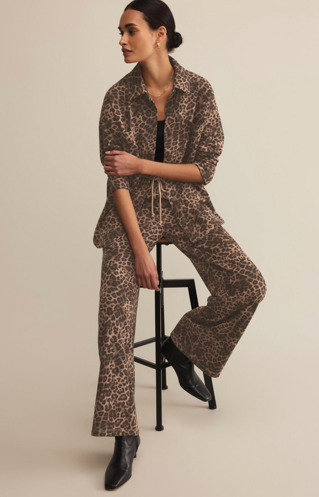 Woman wearing a leopard print outfit sitting on a stool against a beige background