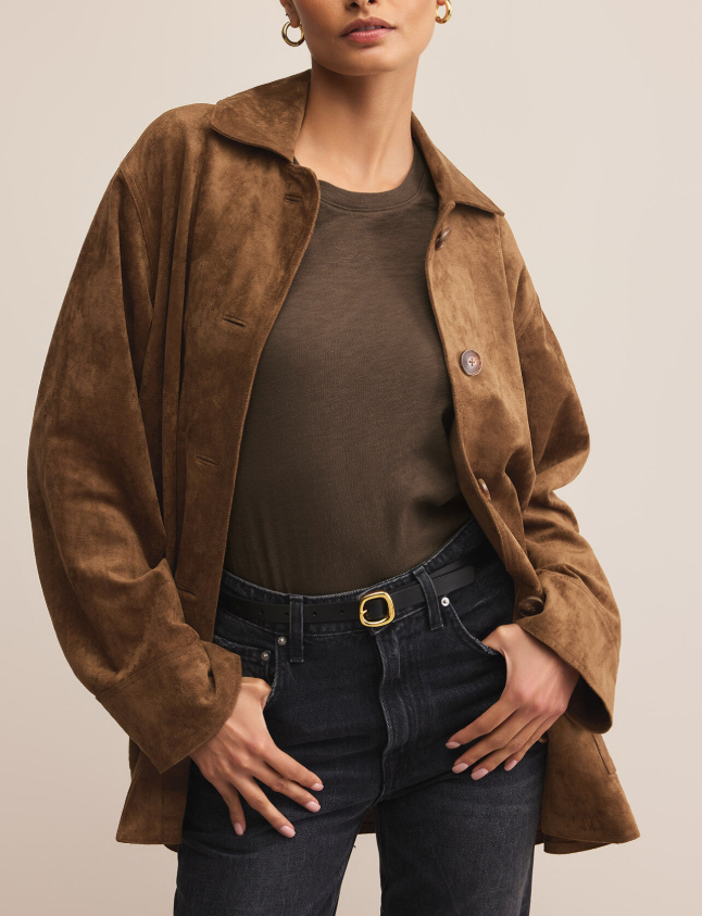 Person wearing a brown faux suede jacket over a dark shirt and jeans on a neutral background