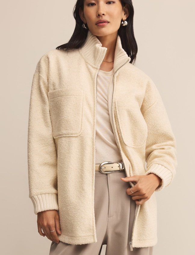 Woman wearing a cream-colored fuzzy zip up coat against a plain background