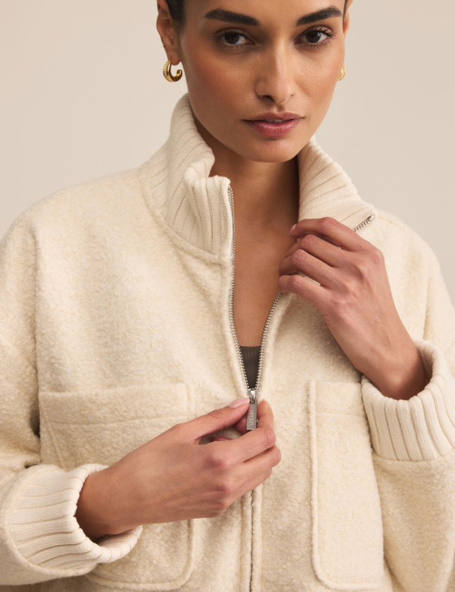 Woman wearing a fuzzy cream-colored zip-up jacket against a neutral background
