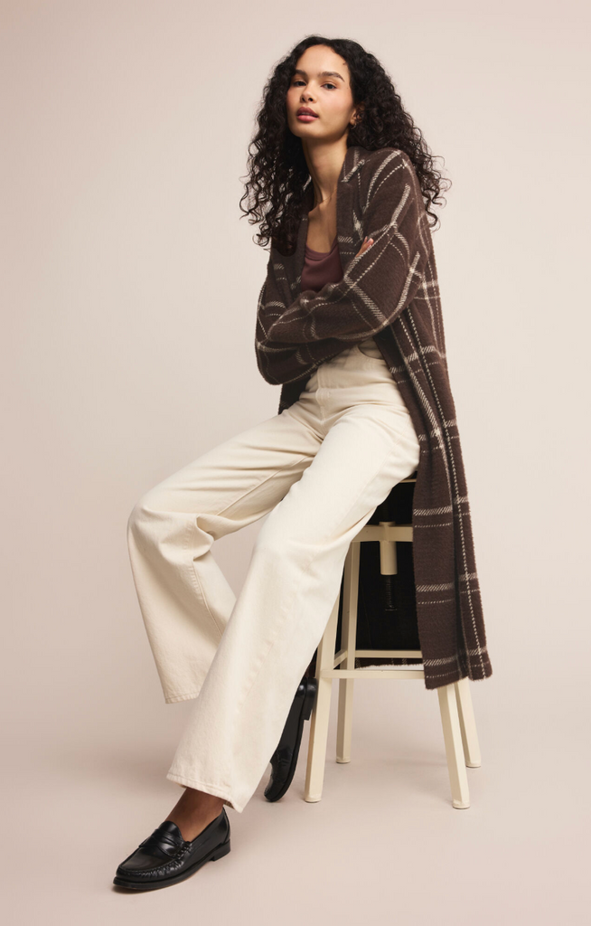 Woman wearing a plaid cardigan, white pants, and black shoes on a beige background