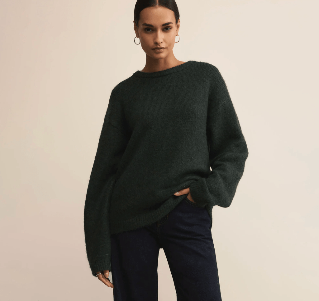 Woman wearing a dark green sweater against a beige background