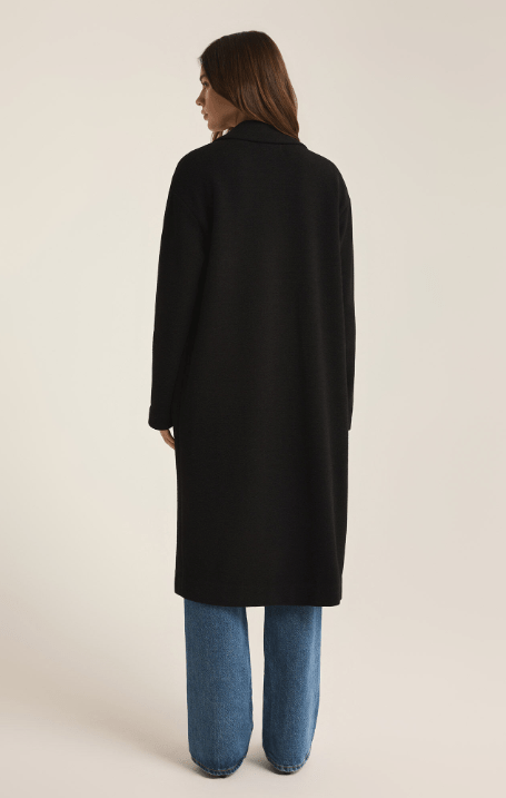 Woman wearing a long black coat and blue jeans on a beige background