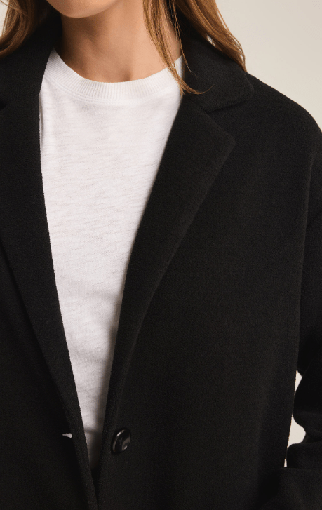 Close up on a woman wearing a long black coat over a white shirt on a neutral background