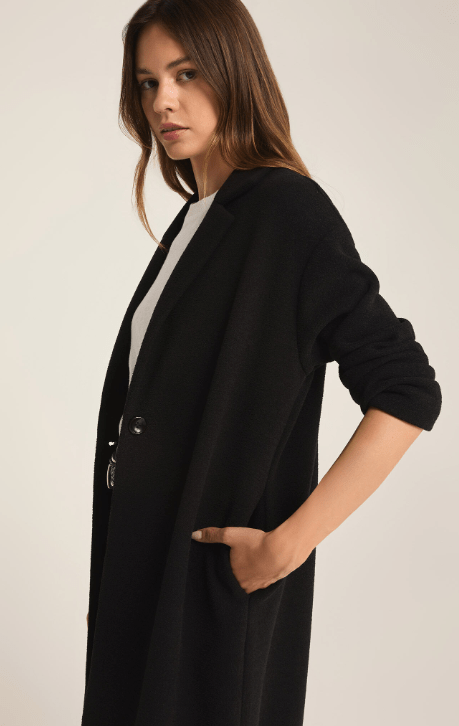 Woman wearing a long black coat against a plain background