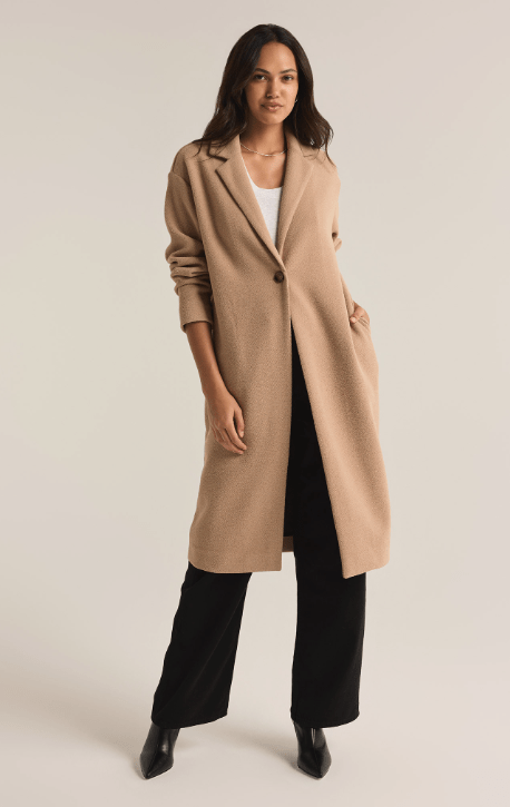 Woman wearing a long beige coat on a plain background